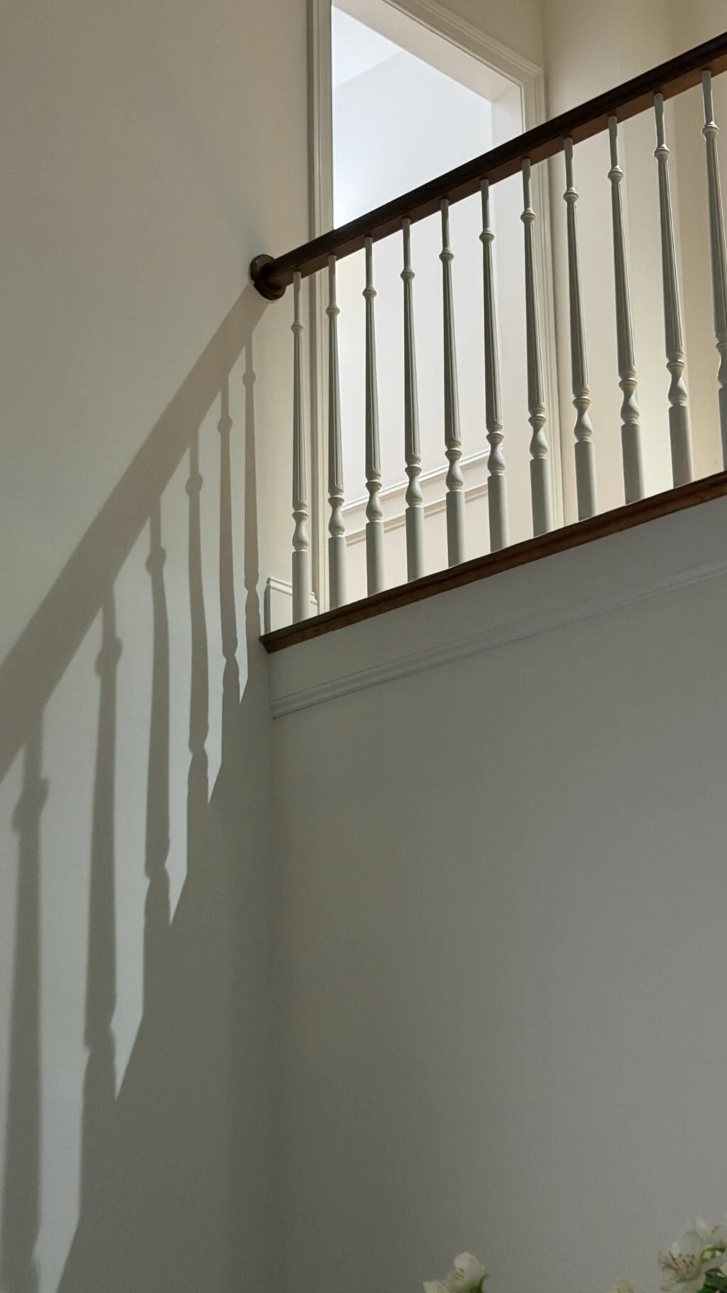 Staircase railing casting elongated shadows of the balusters on a wall, creating the illusion of a larger set of balusters that does not exist.
