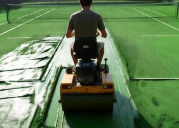Young man riding a green motorized clay tennis court roller early in the morning, repairing wet courts after a rainstorm – illustrating Dave Kurlan’s “do whatever it takes” mindset from his sales mastery story